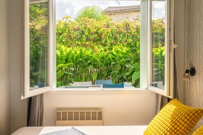 Un dormitorio con vista a un jardín exuberante, una cama con un almohadón amarillo y un radiador.