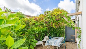 A patio with a table and chairs, surrounded by lush greenery and a wooden pergola. - Holiday Home 'Du Porche' with Private Terrace and Wi-Fi (Chaillevette)