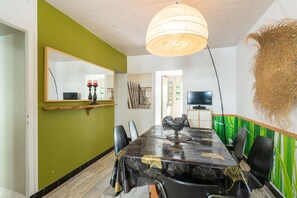 Comedor con mesa, sillas, una araña, televisor y una pared con detalles en verde.