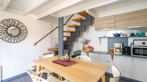 Eine moderne Küche mit einer Holztreppe, einem Essbereich mit Holztisch und weißen Stühlen sowie einem dekorativen Spiegel an der Wand.