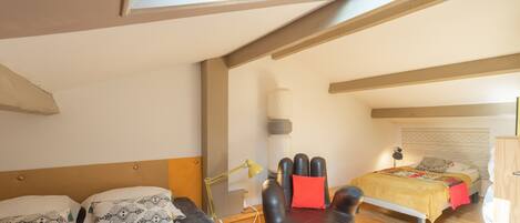 A bedroom with a skylight, two beds, a sofa, and a lamp.