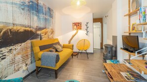 Ein Wohnzimmer mit Sofa, Sessel, Tisch, Bücherregal und einem Bild an der Wand.