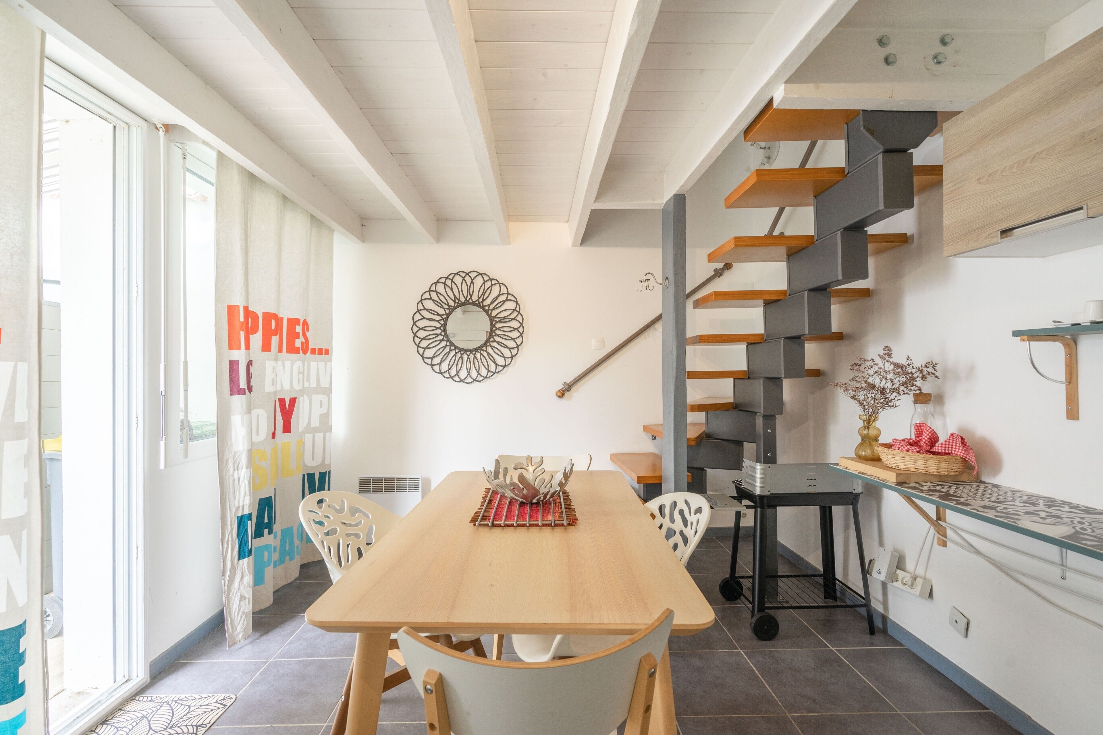 A modern kitchen with a wooden table, chairs, a decorative wall piece, and a staircase.