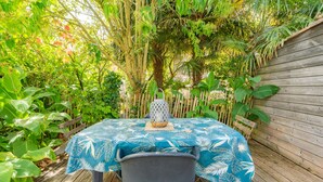 Ein Tisch mit blauer Tischdecke, ein Stuhl und ein Laterne auf einem Holzdeck, umgeben von üppiger Vegetation.