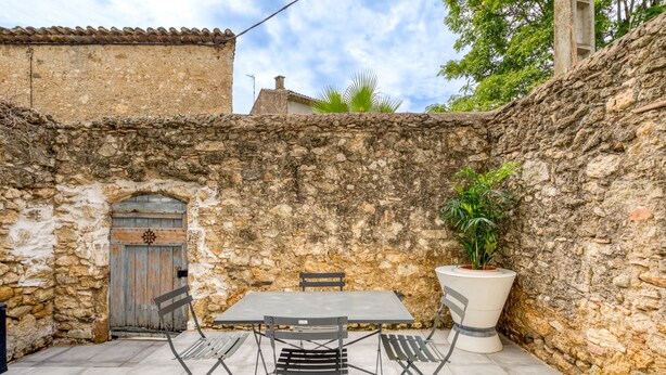 A stone-walled courtyard with a table and chairs, a door, and a potted plant. - Apartment 'Le Poulailler D'alice' with Private Terrace, Wi-Fi and Air Conditioning (Saint-Génies-de-Fontedit)