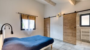 A bedroom with a bed, a window with curtains, a wall-mounted light, and a sliding door. - Apartment 'Le Poulailler D'alice' with Private Terrace, Wi-Fi and Air Conditioning (Saint-Génies-de-Fontedit)