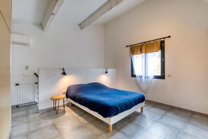 A bedroom with a single bed, a small table, a radiator, and a window with curtains.