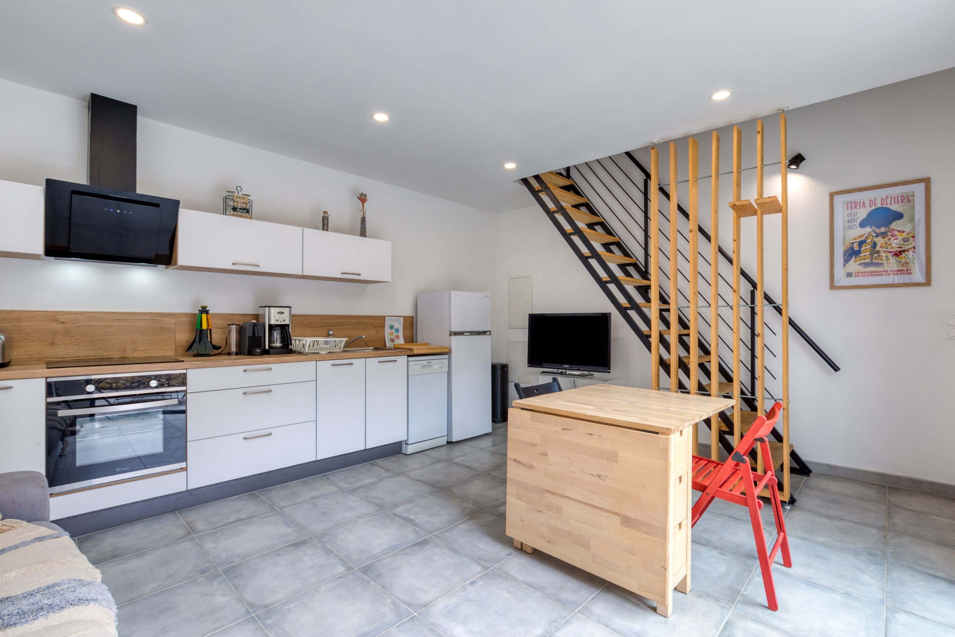 Une cuisine moderne avec des meubles blancs, une table en bois et une chaise rouge.