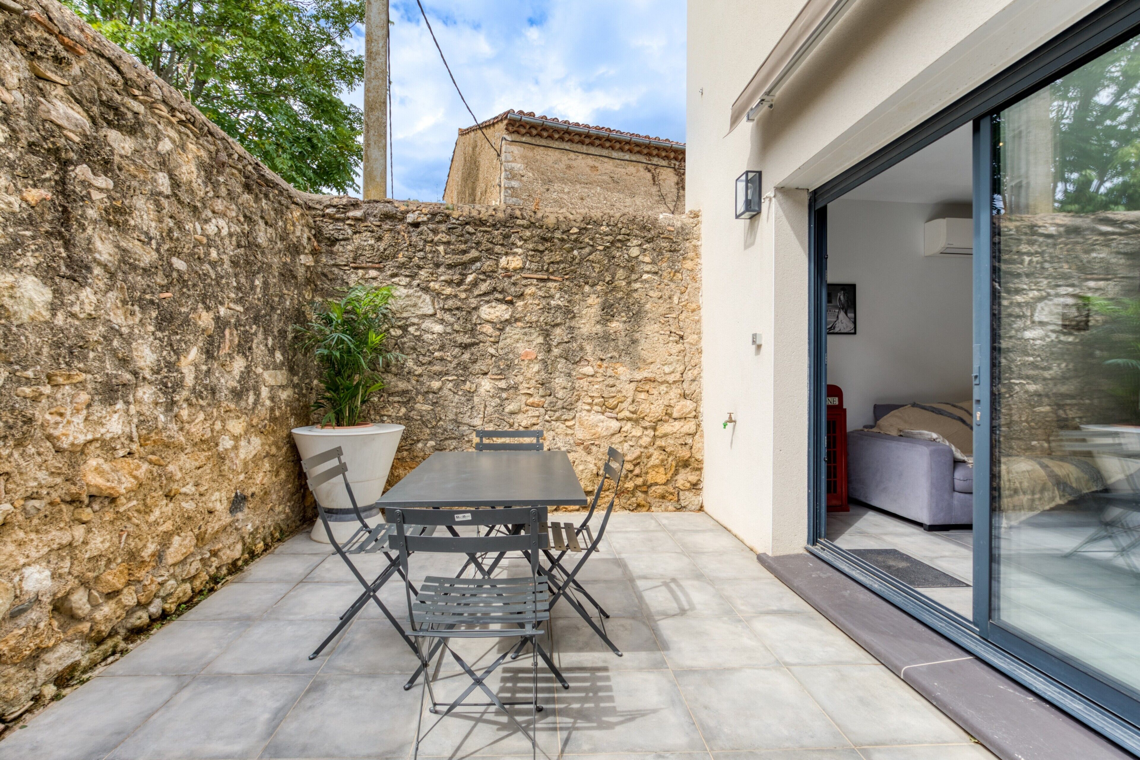 A patio with a table and chairs, a potted plant, and a stone wall.