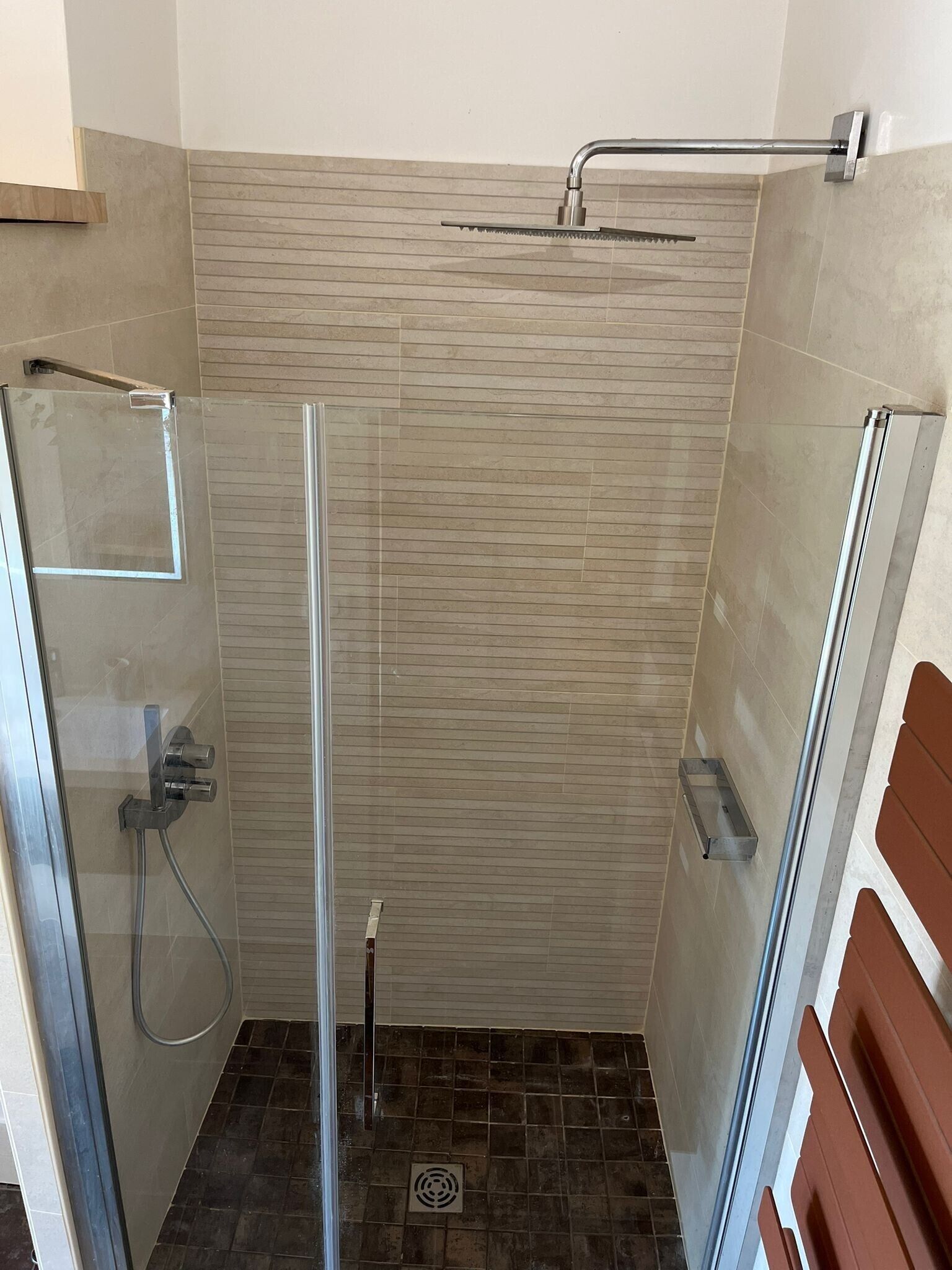 A glass-enclosed shower with a handheld showerhead, a towel rack, and a small shelf.