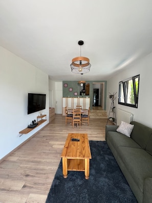 Un salon moderne comprenant un téléviseur, une table basse en bois, un canapé et un coin repas avec des chaises et une table.