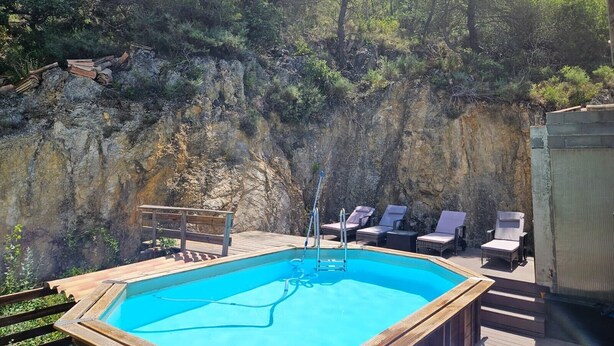 An outdoor swimming pool with a wooden deck, lounge chairs, and a rocky cliff backdrop.
