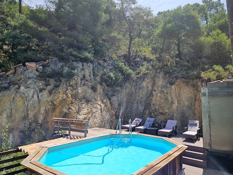 An outdoor swimming pool with a wooden deck, lounge chairs, and a rocky cliff backdrop.