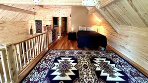 A loft-style bedroom with exposed wooden beams, a patterned rug, a bed, and a nightstand. - Explore more. Relax More. Escape to the mountains! (Cimarron)