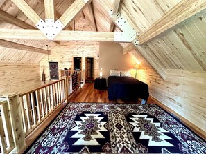 Une chambre de style « loft », avec des poutres en bois apparentes, un tapis à motifs, un lit et une table de chevet.