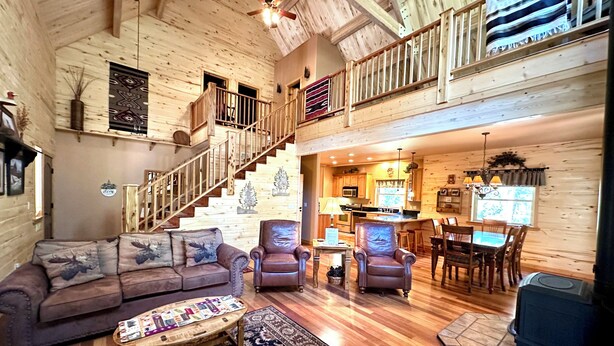A spacious living area with a wooden staircase, a dining set, and a kitchen in a log cabin. - Explore more. Relax More. Escape to the mountains! (Cimarron)