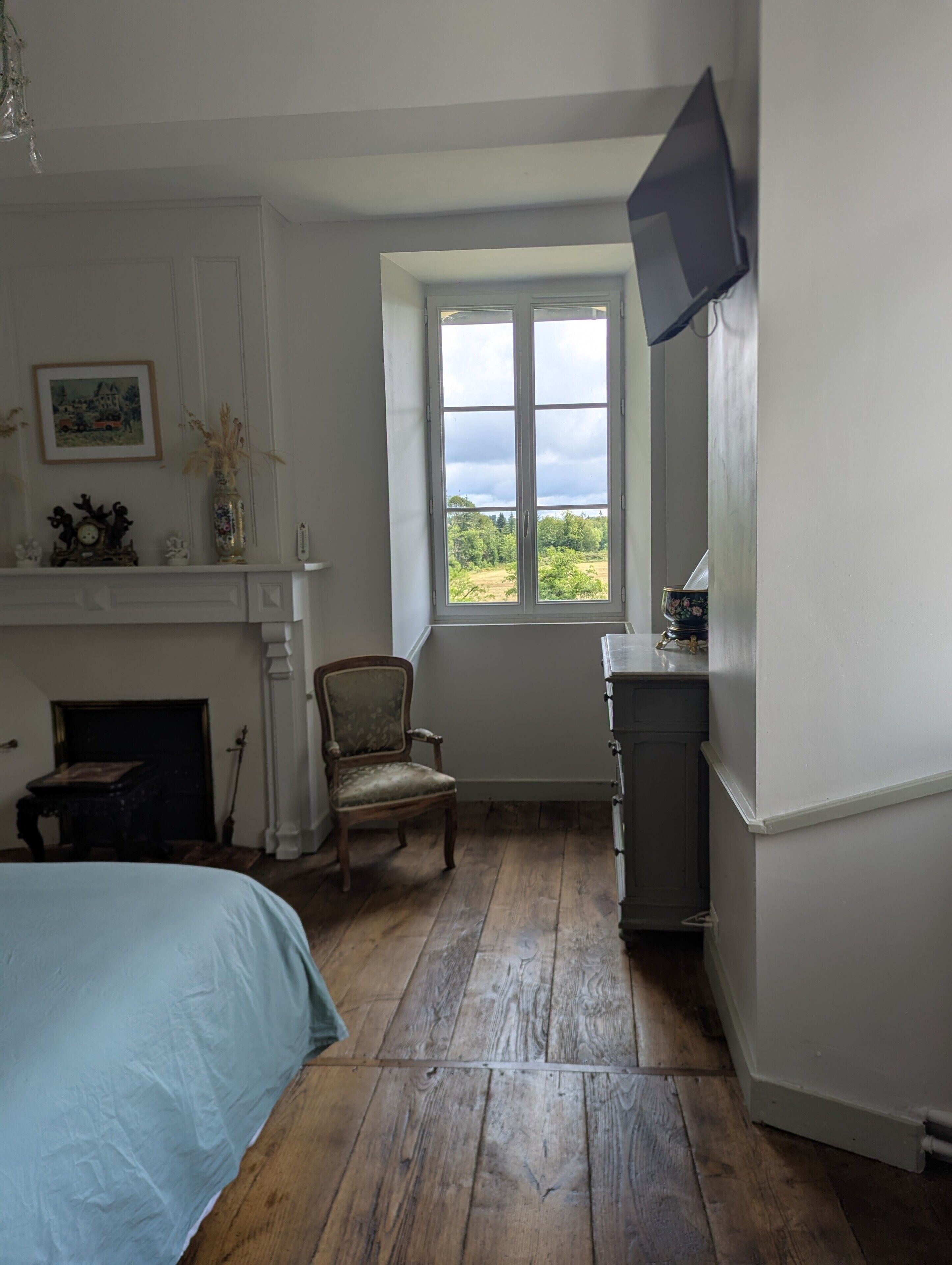 Une chambre à coucher comprenant un lit, une chaise, une cheminée, un téléviseur et une fenêtre donnant sur un paysage verdoyant.