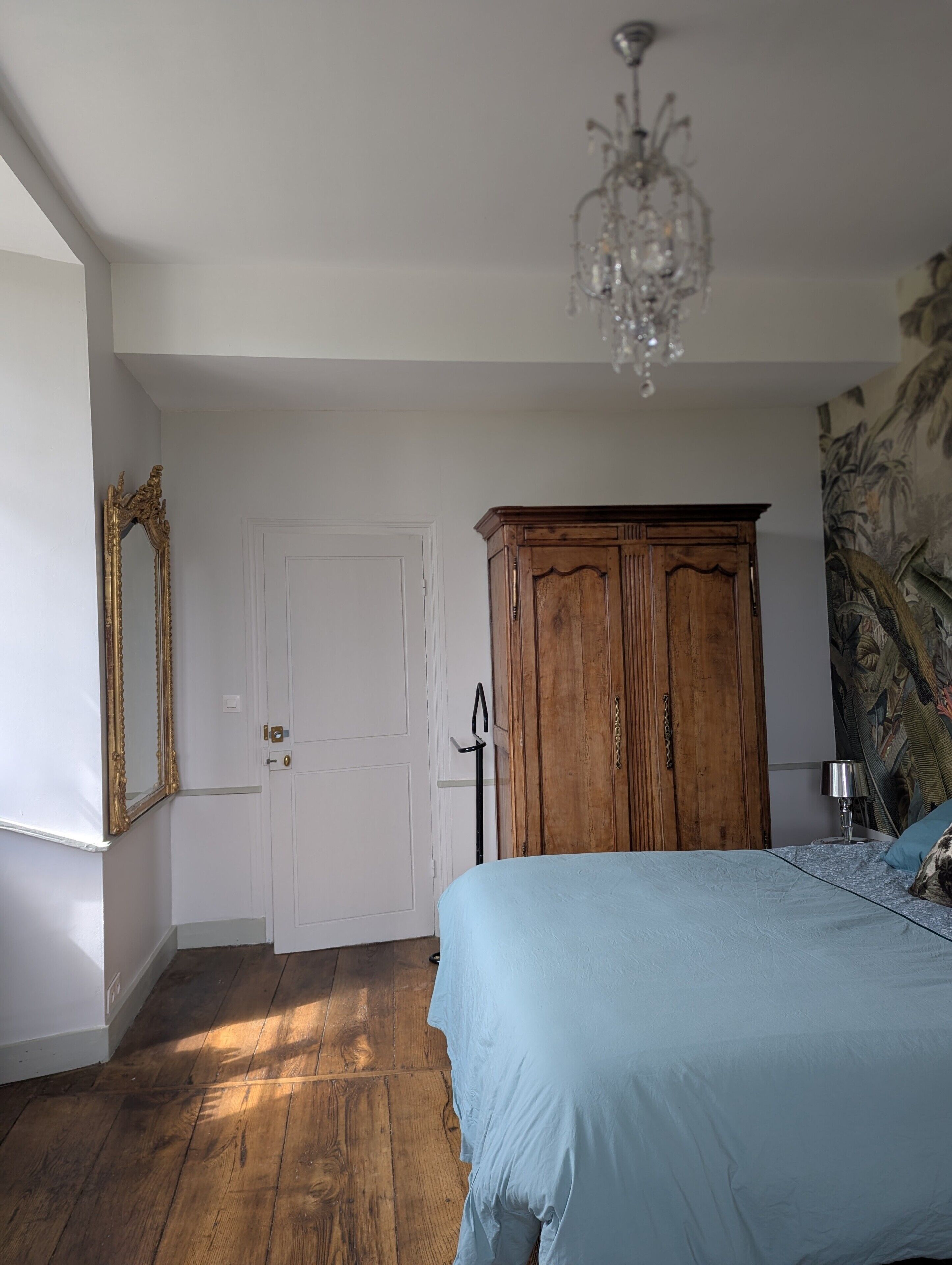 Une chambre à coucher avec un lit, une armoire en bois, une porte et un lustre.