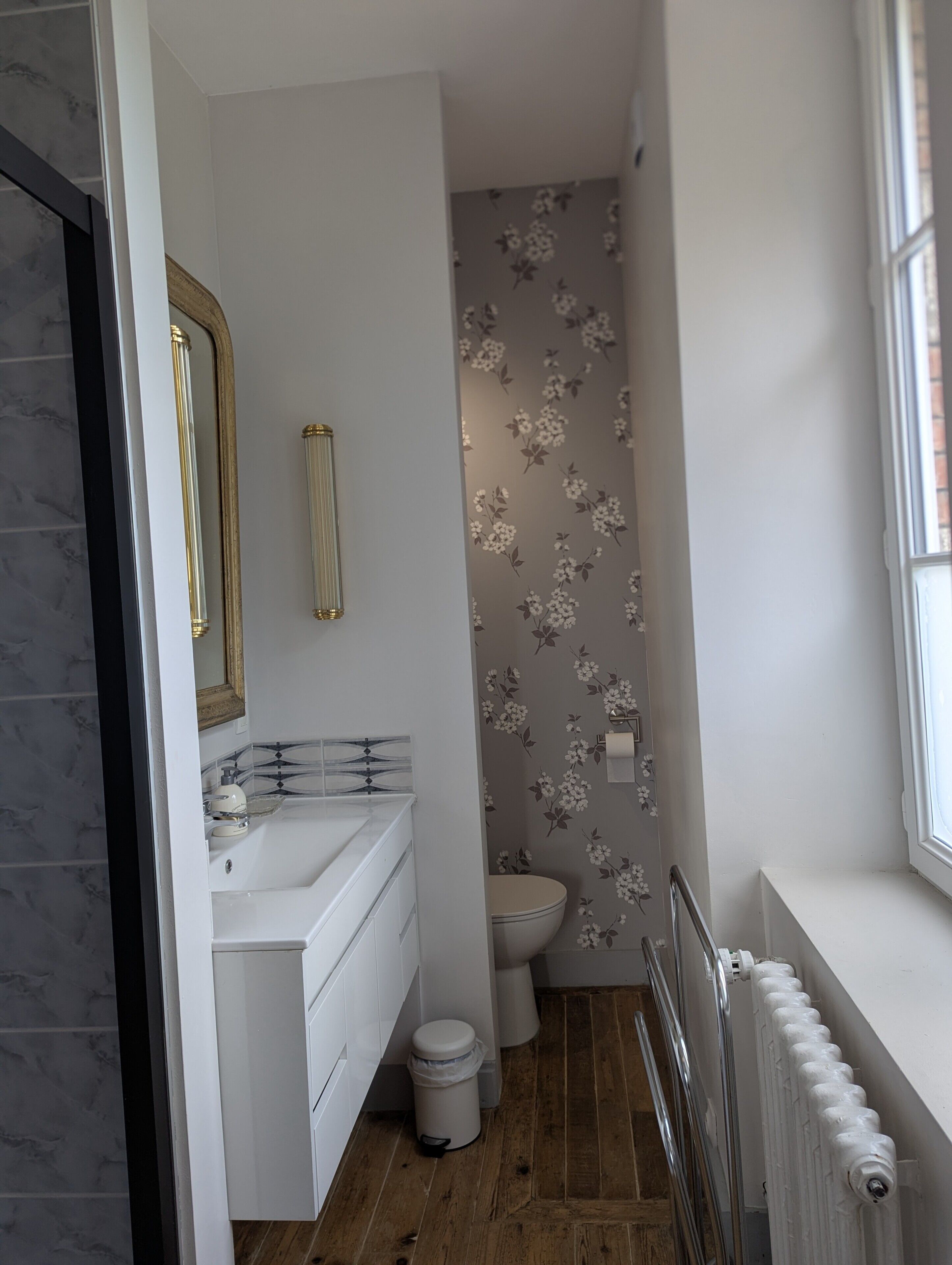 Une salle de bain avec un lavabo blanc, un miroir et des toilettes, un radiateur et une fenêtre.