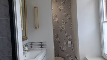 Une salle de bain avec un lavabo blanc, un miroir et des toilettes, un radiateur et une fenêtre.