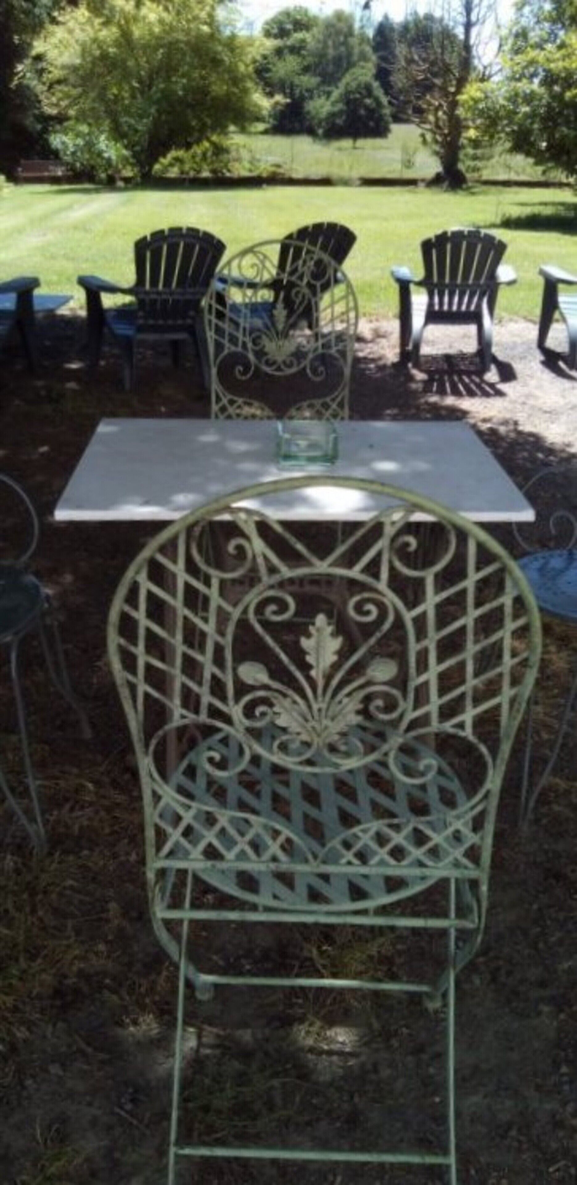 Espace extérieur aménagé avec des chaises et une table en métal, entouré d’une pelouse et d’arbres.