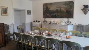 Une salle à manger avec une longue table, des chaises, un tableau et un buffet blanc agrémenté d’objets décoratifs.