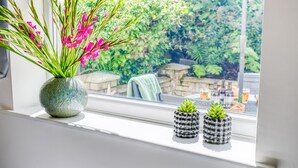 Una ventana con un florero de flores rosas y dos pequeñas suculentas en el alféizar.