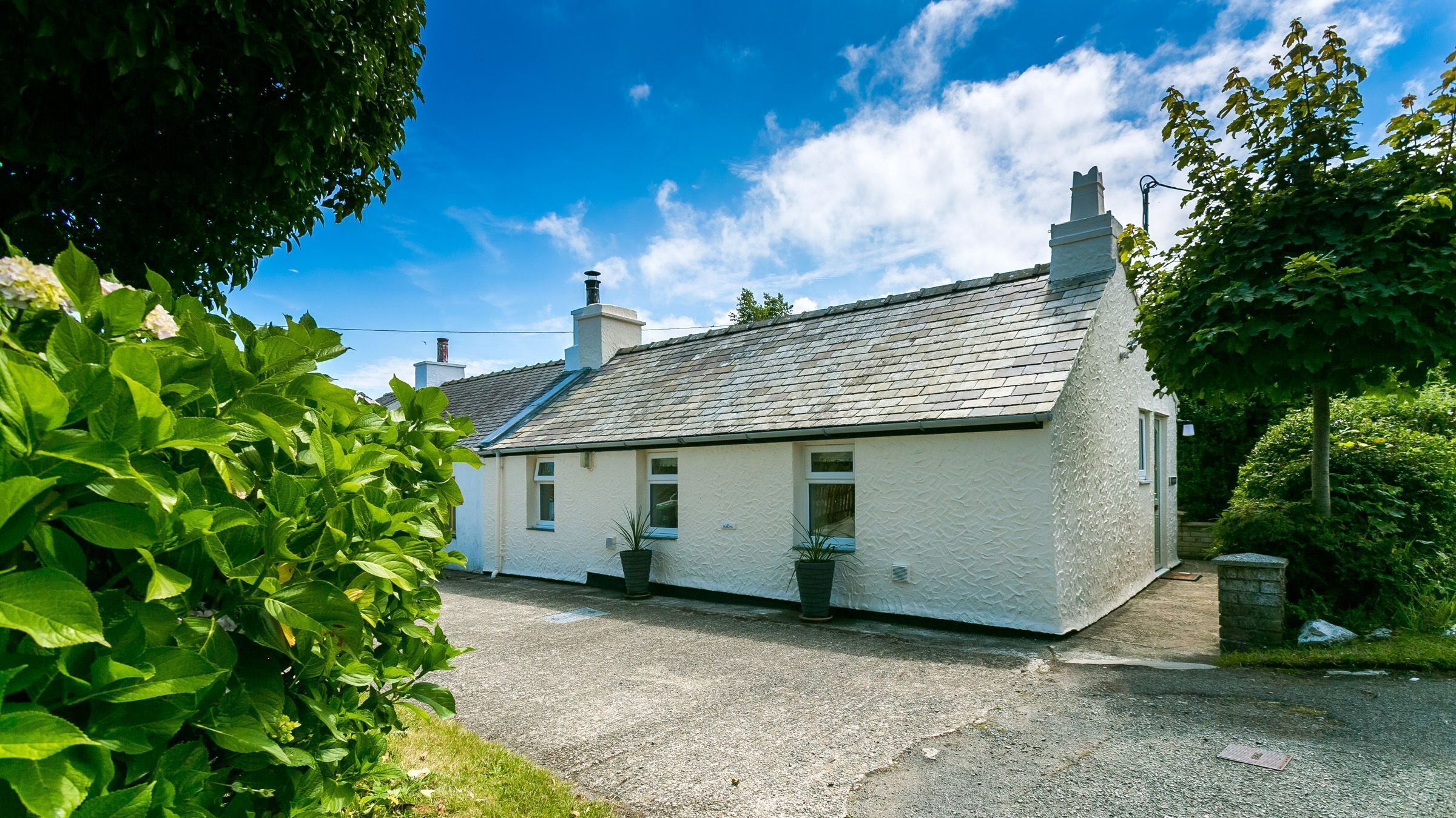 A white house with a grey roof, a chimney, and a gravel driveway.