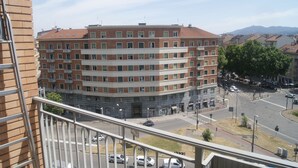 A multi-story building with a brick facade and a flat roof, located near a street intersection with visible cars and a pedestrian crossing.