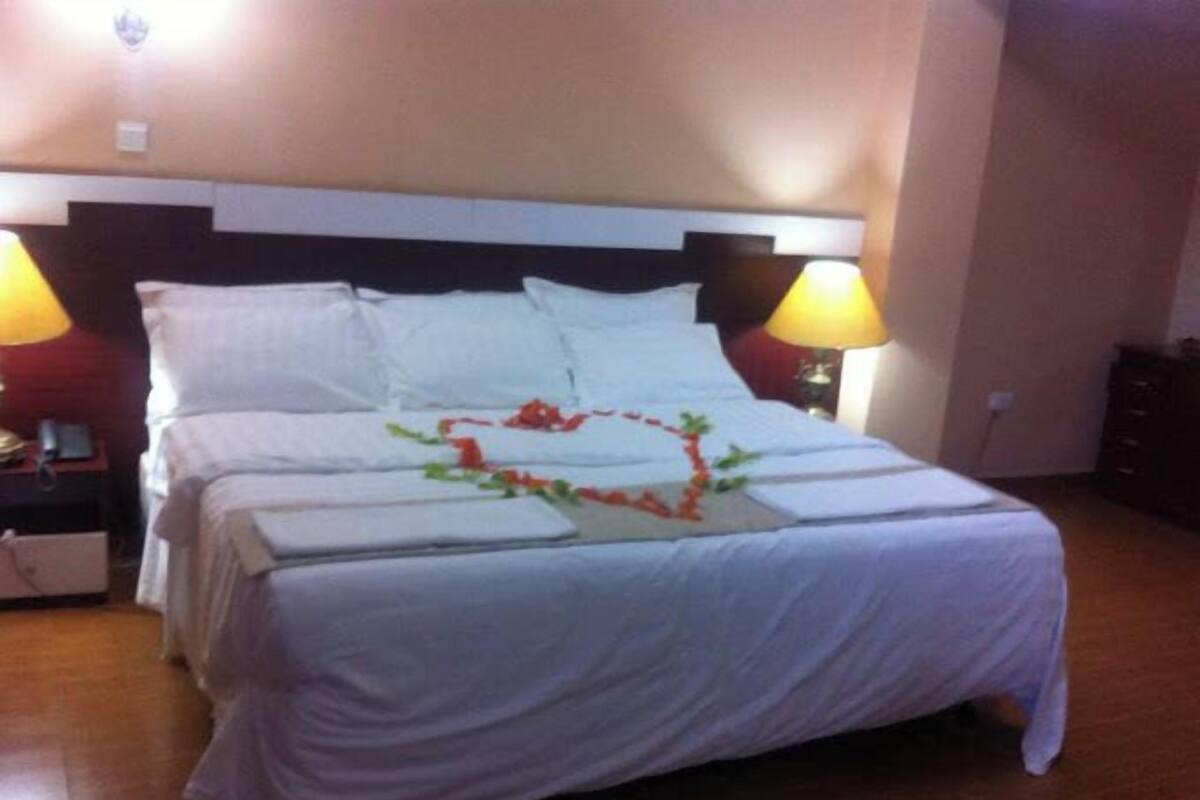 A neatly made bed with white linens and a heart-shaped decoration on the bedspread.