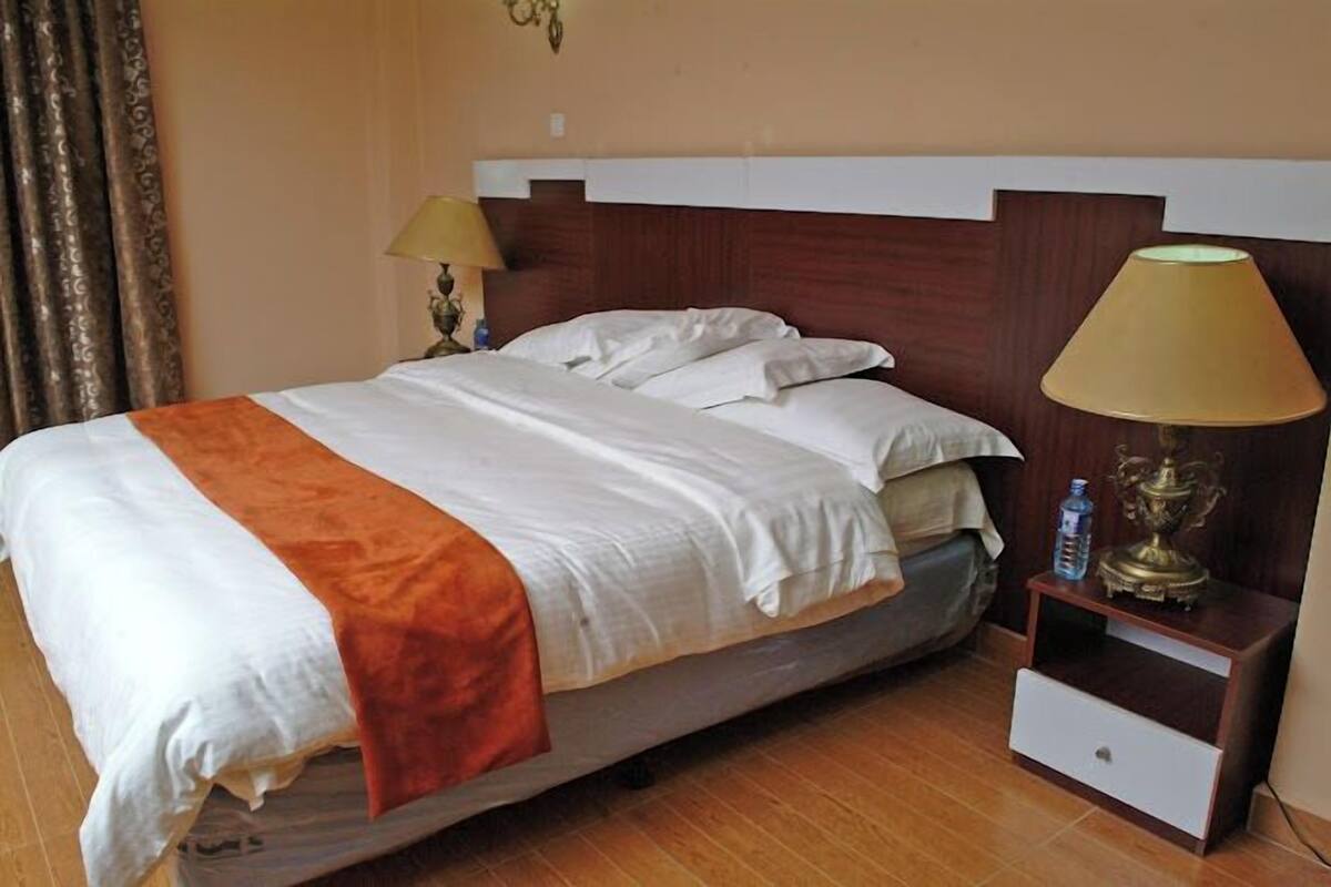 A hotel room with a bed, two bedside lamps, a nightstand, and a water bottle.