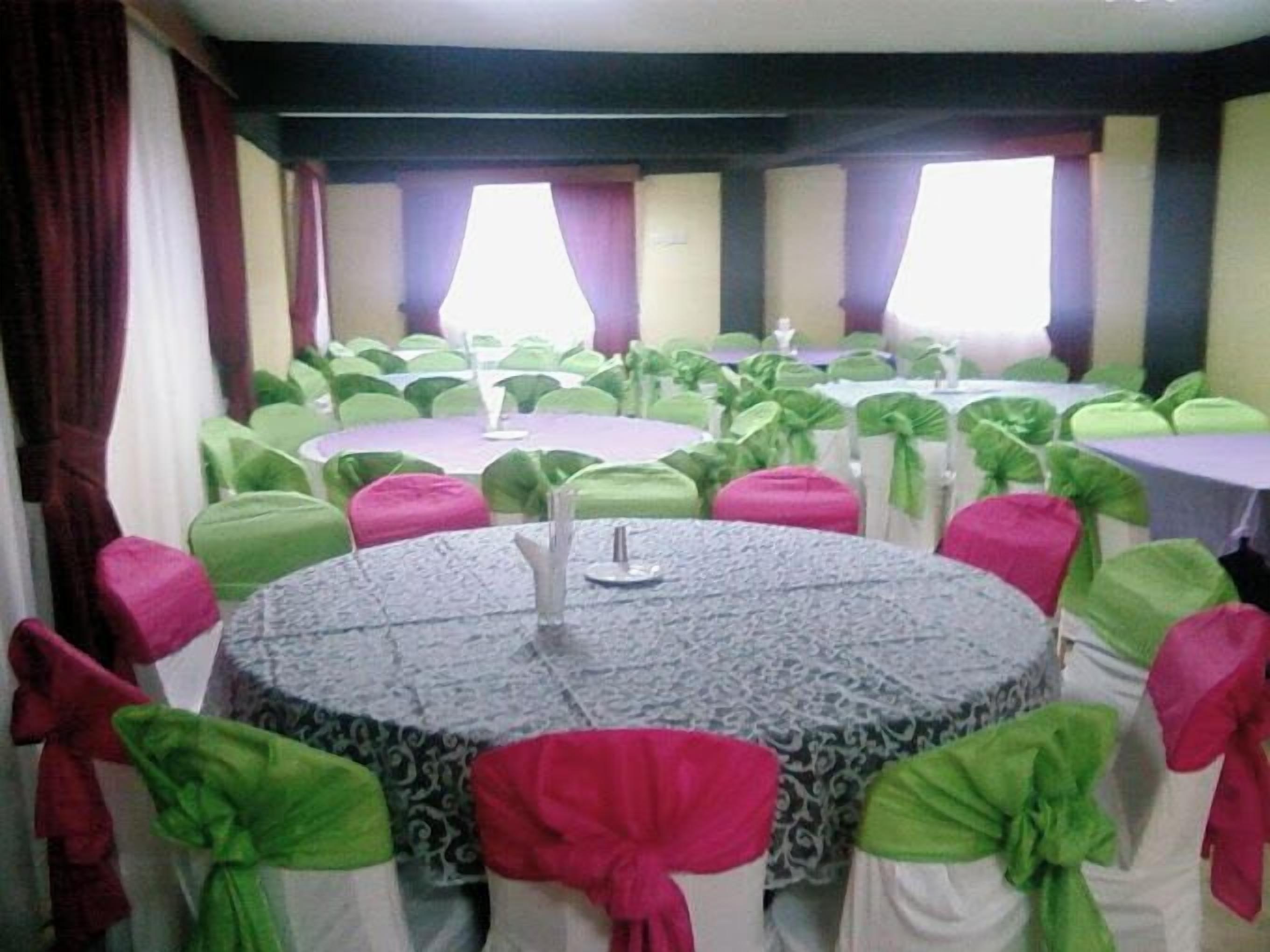 A conference room with round tables, green and pink chair sashes, and a patterned tablecloth.