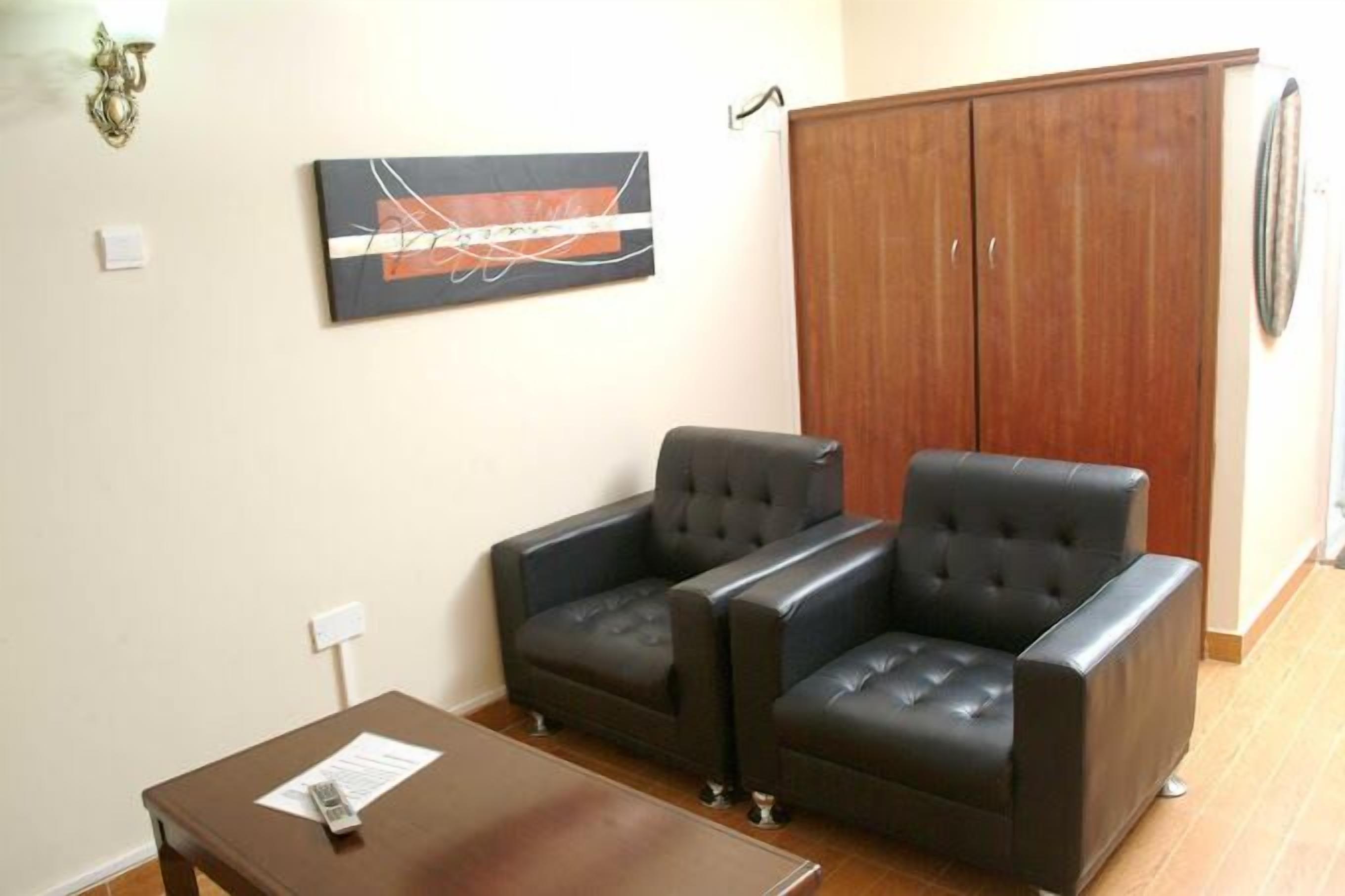 Un salon avec deux canapés en cuir noir, un meuble en bois et un tableau accroché au mur.