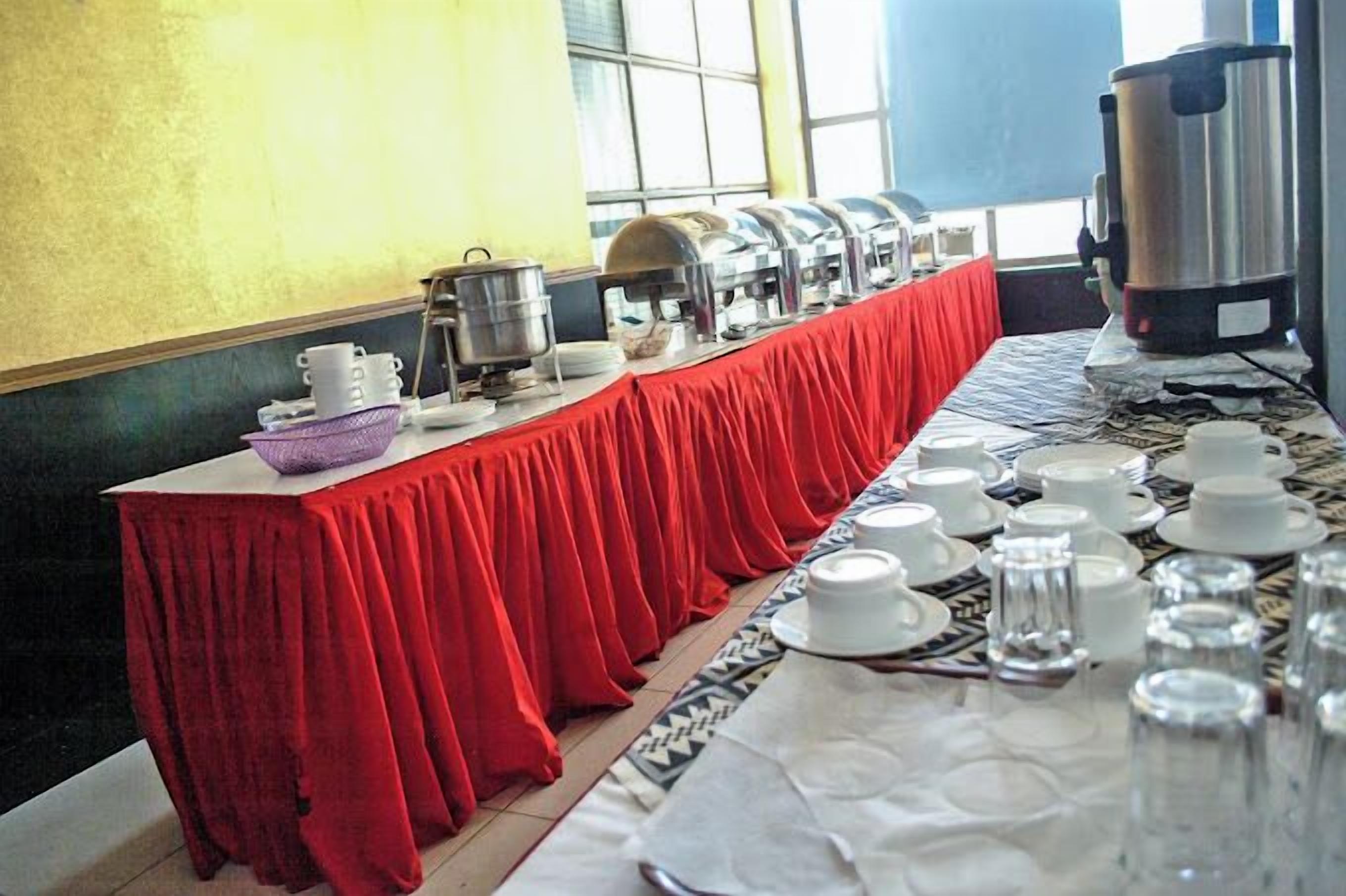 A buffet setup with a long table covered in a red tablecloth, equipped with various serving dishes and utensils.