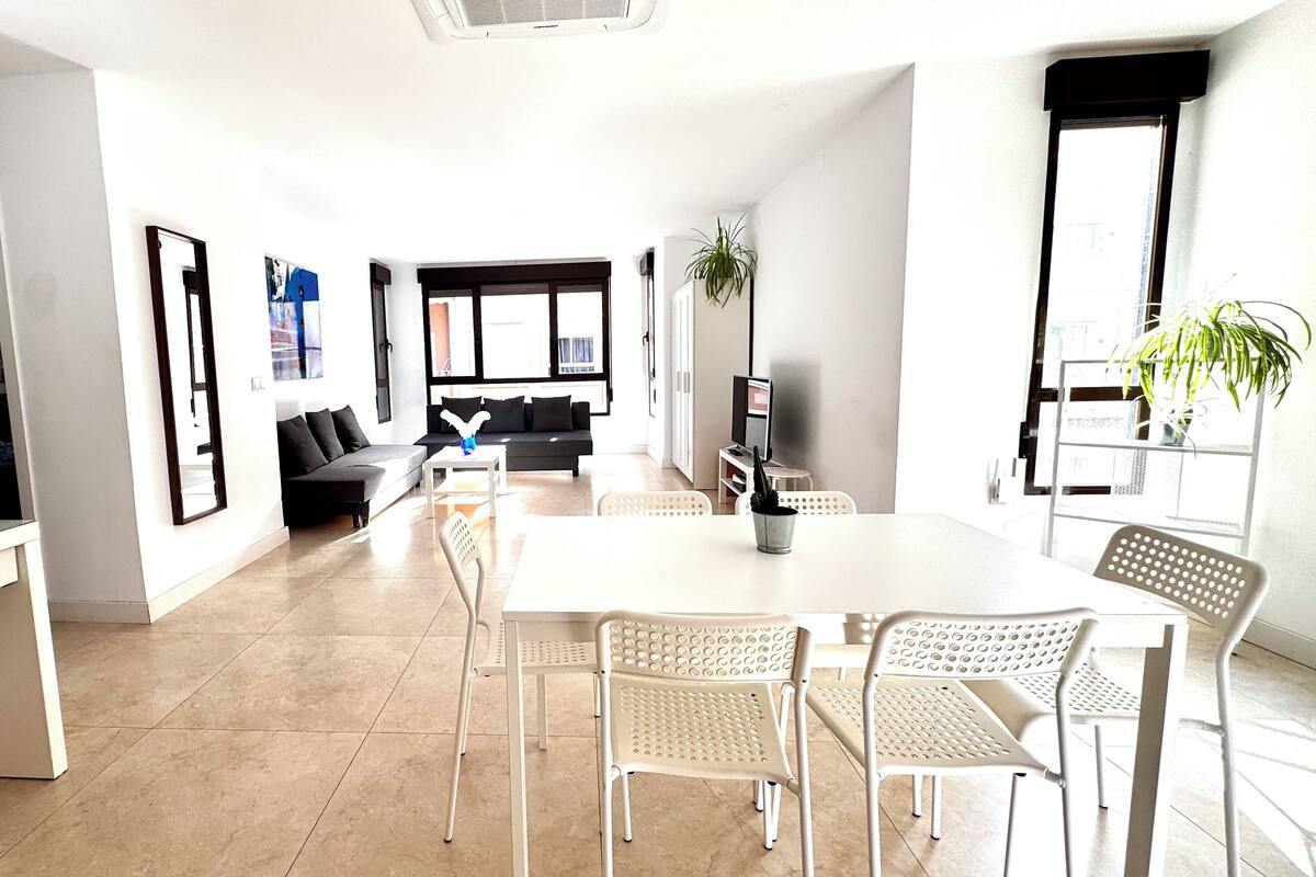 A modern living room with a sofa, a coffee table, and a TV. There is a dining area with a table and chairs.