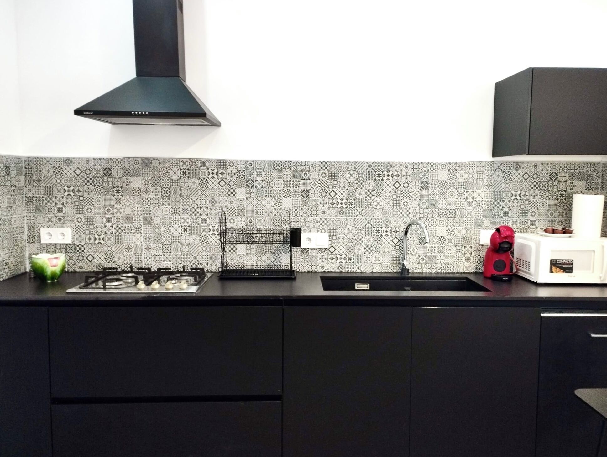 Una cocina con un salpicadero decorativo, una estufa a gas, un lavaplatos y un microondas compacto.
