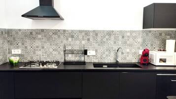 Una cocina con un salpicadero decorativo, una estufa a gas, un lavaplatos y un microondas compacto.
