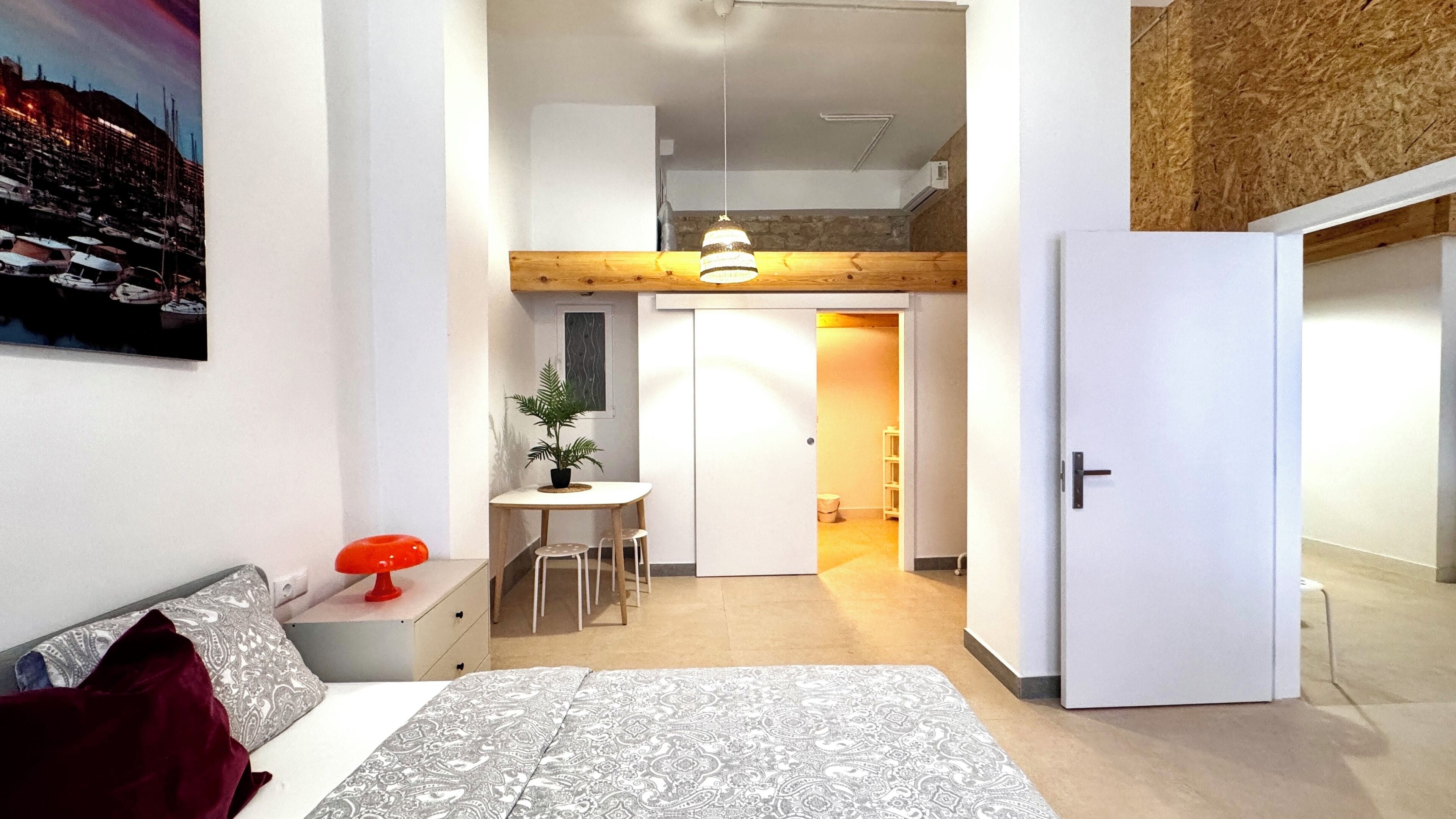 Un dormitori modern amb un llit, un escriptori i una cadira. Hi ha una porta que condueix a una altra habitació.
