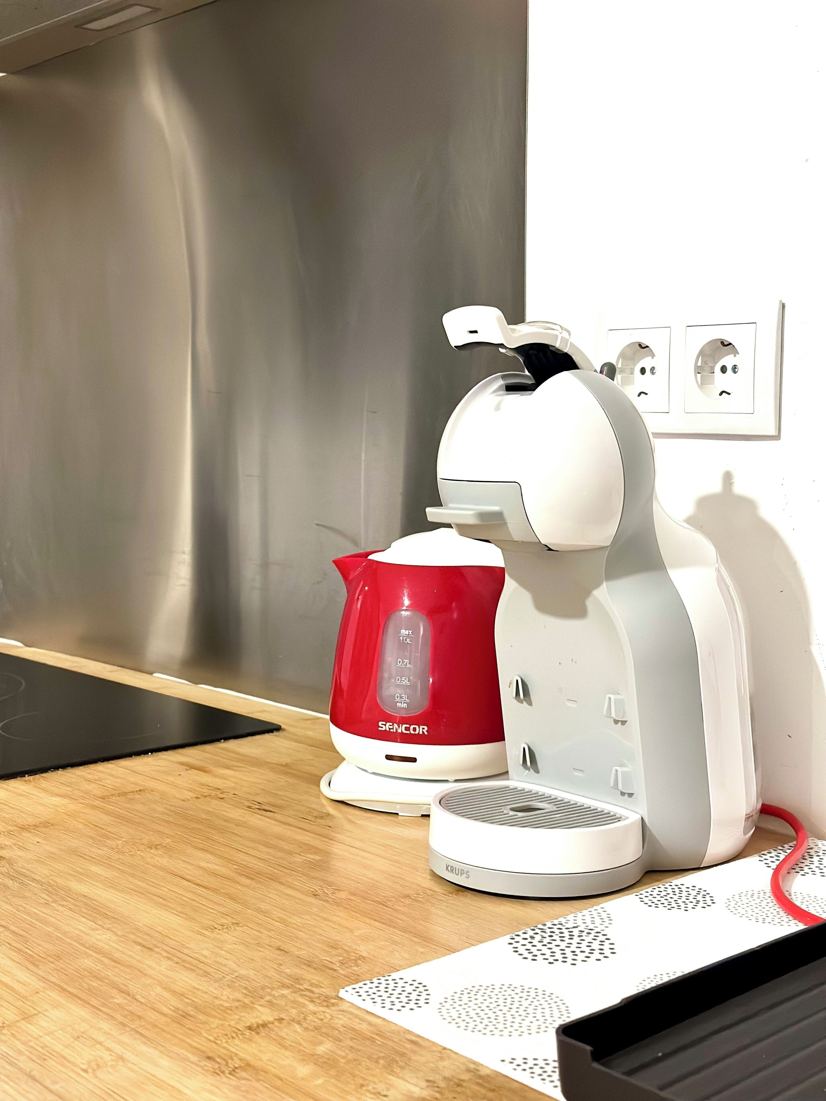 Eine Küche mit Dunstabzugshaube aus Edelstahl, einem roten und weißen Wasserkocher und einer weißen Kaffeemaschine auf einer Holzausziehtafel.
