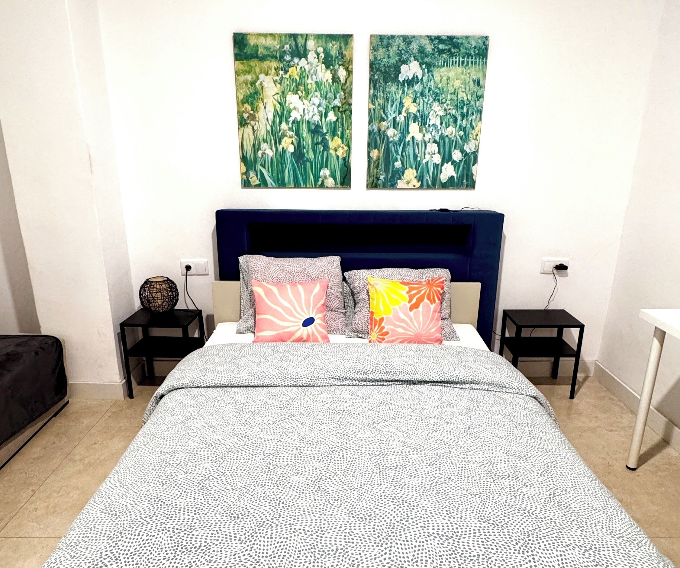Un dormitorio con cama, dos mesitas de noche, un aparador y dos cuadros en la pared.