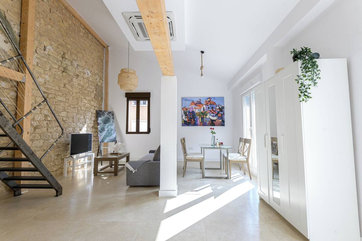 A spacious living area with a stone wall, a staircase, a sofa, a dining table, and a painting.