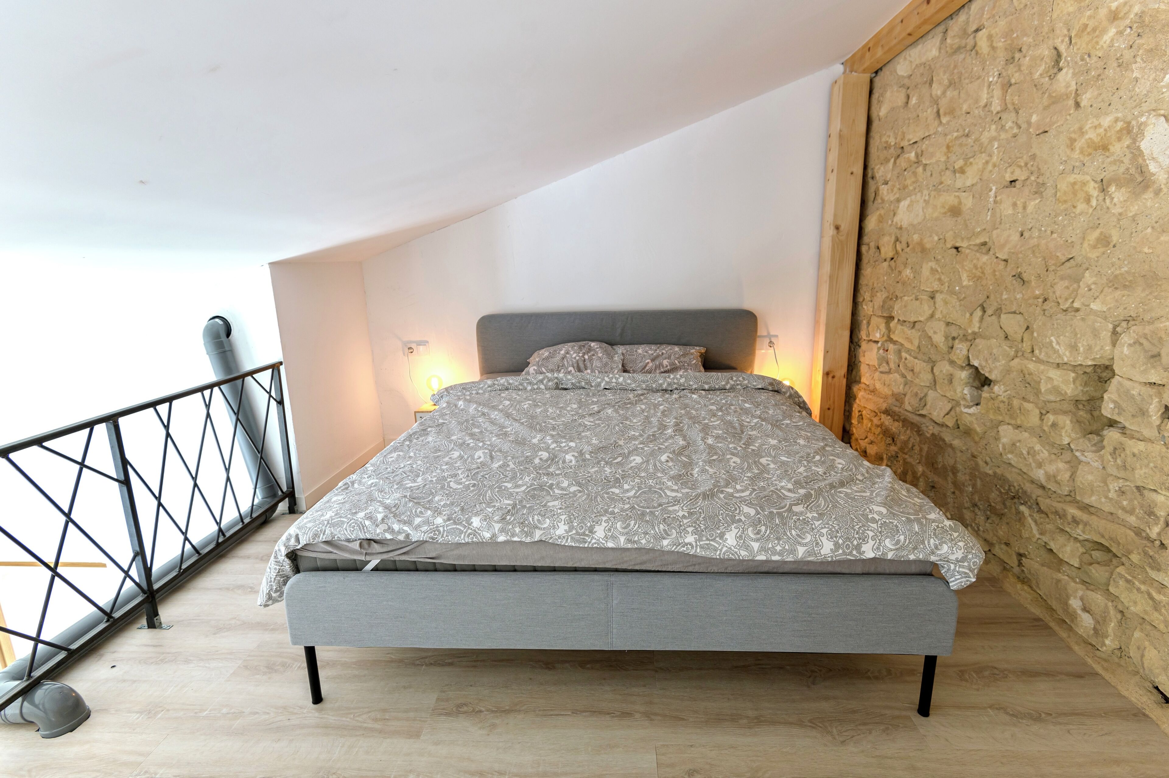 Quarto com cama, parede de pedra e guarda-corpo de varanda.