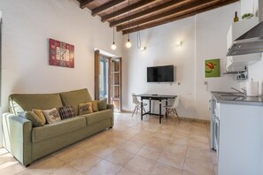Una sala de estar con un sofá, una mesa de comedor, un televisor y una zona de cocina.