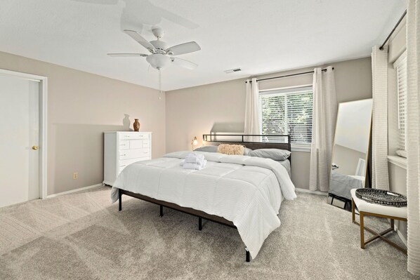Une chambre à coucher comprenant un lit, une commode, un miroir et un ventilateur de plafond.