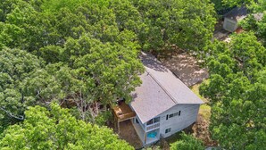 Une maison de plain-pied entourée d’arbres denses, avec un petit porche et un garage bien visible.