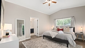 Une chambre à coucher comprenant un lit, une table de chevet, une commode, un ventilateur de plafond et une fenêtre avec des rideaux.