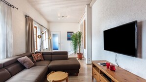 Un salon moderne avec un canapé d’angle, un téléviseur, des meubles en bois et une plante en pot.