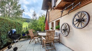 Une terrasse avec un barbecue, des chaises en bois et une table.