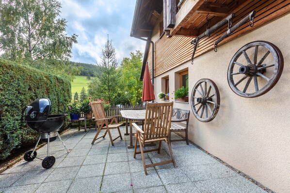 Une terrasse avec un barbecue, des chaises en bois et une table.