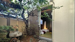 Ein traditioneller japanischer Raum mit Tatami-Bodenbelag, einem niedrigen Tisch und einer Schiebetür zu einer privaten Fläche.